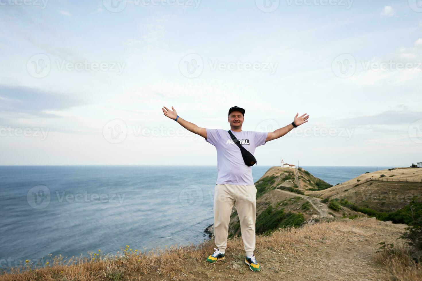 stilig ung man med vapen utsträckt stående på topp av en berg mot hav. cape emine, svart hav kust, bulgarien. foto