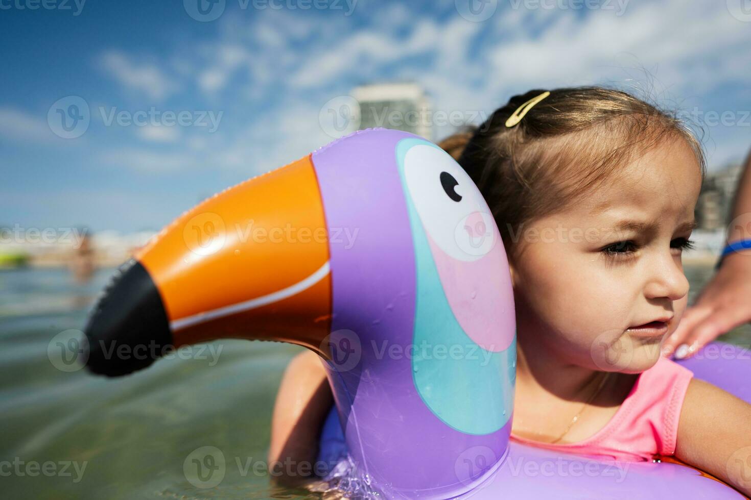 liten flicka simning i de hav med uppblåsbar ringa tycka om toucan i sommar dag. foto