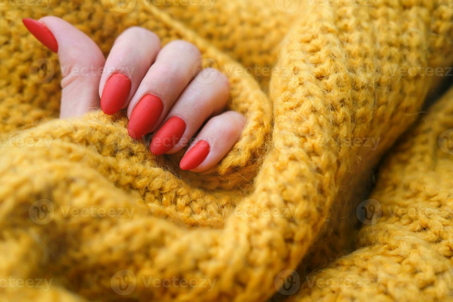 kvinnors händer med en skön matt oval manikyr i en värma orange stickat Tröja. vinter- trend, omslag röd naglar med gel putsa, schellack. foto