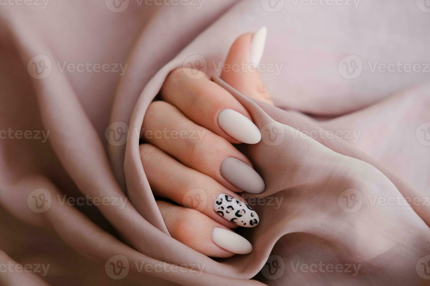 en kvinnas hand med en skön manikyr är innehav en silke tyg. höst trend, beige Färg putsning med leopard mönster på naglar med gel putsa, schellack. kopia Plats. foto