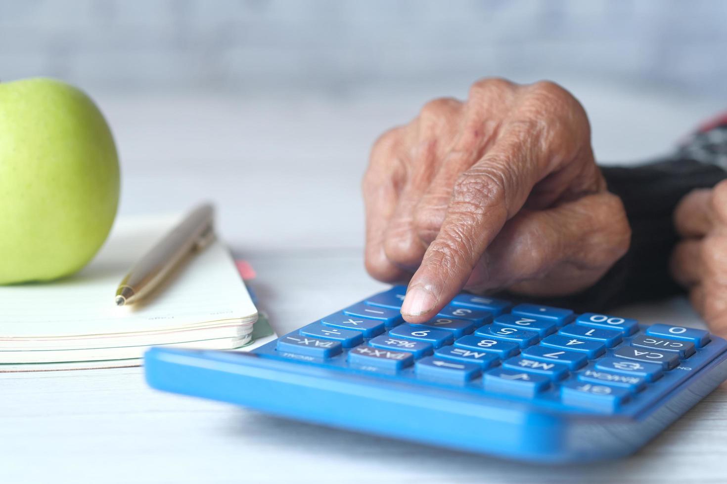 äldre kvinnor räcker med hjälp av miniräknare på skrivbordet foto