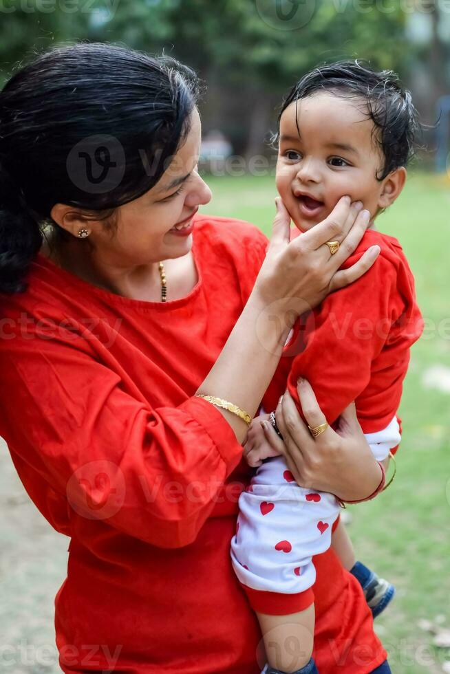 kärleksfull mamma bärande av henne bebis på samhälle parkera. ljus porträtt av Lycklig mamma innehav barn i henne händer. mor kramas henne liten 9 månader gammal son. foto