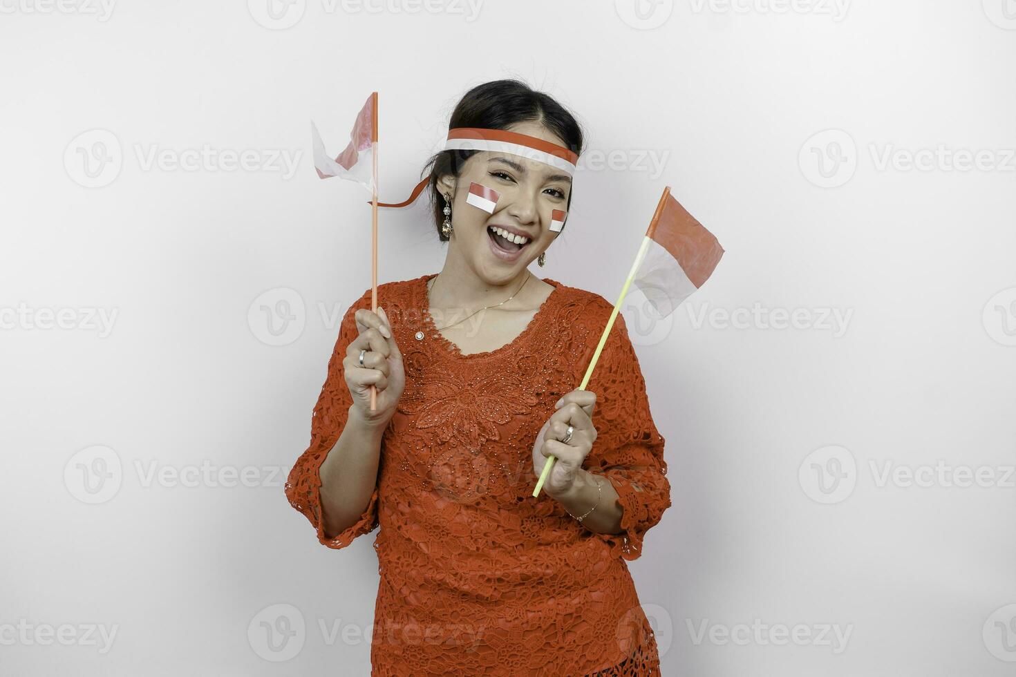 Lycklig leende indonesiska kvinna bär röd kebaya och pannband innehav Indonesiens flagga till fira indonesien oberoende dag isolerat över vit bakgrund. foto