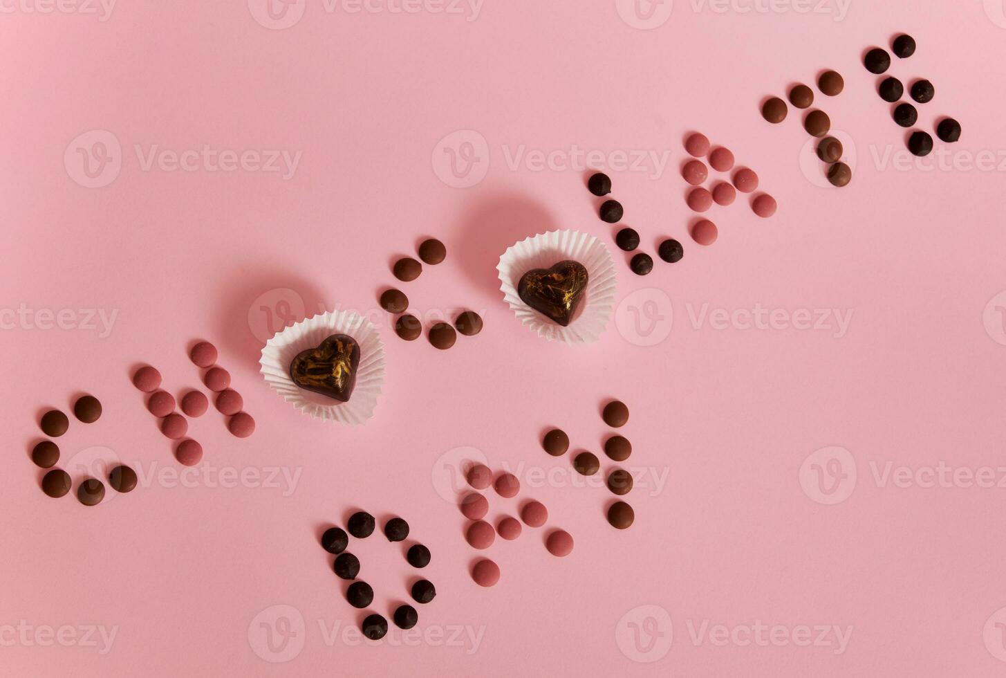 choklad dag text lagd ut från mång färgad choklad piller och praliner på rosa bakgrund med kopia Plats foto