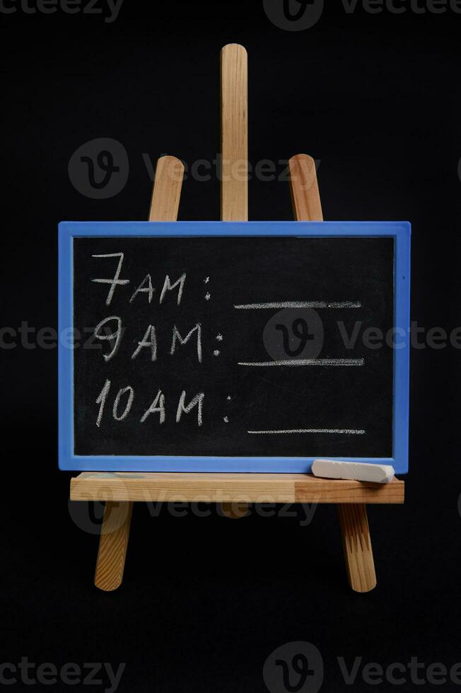 text schema med en vit krita, på en svarta tavlan stående på en trä- tabell staffli, isolerat över svart bakgrund med kopia Plats. planera koncept, tid förvaltning, tidtabell och timing. foto