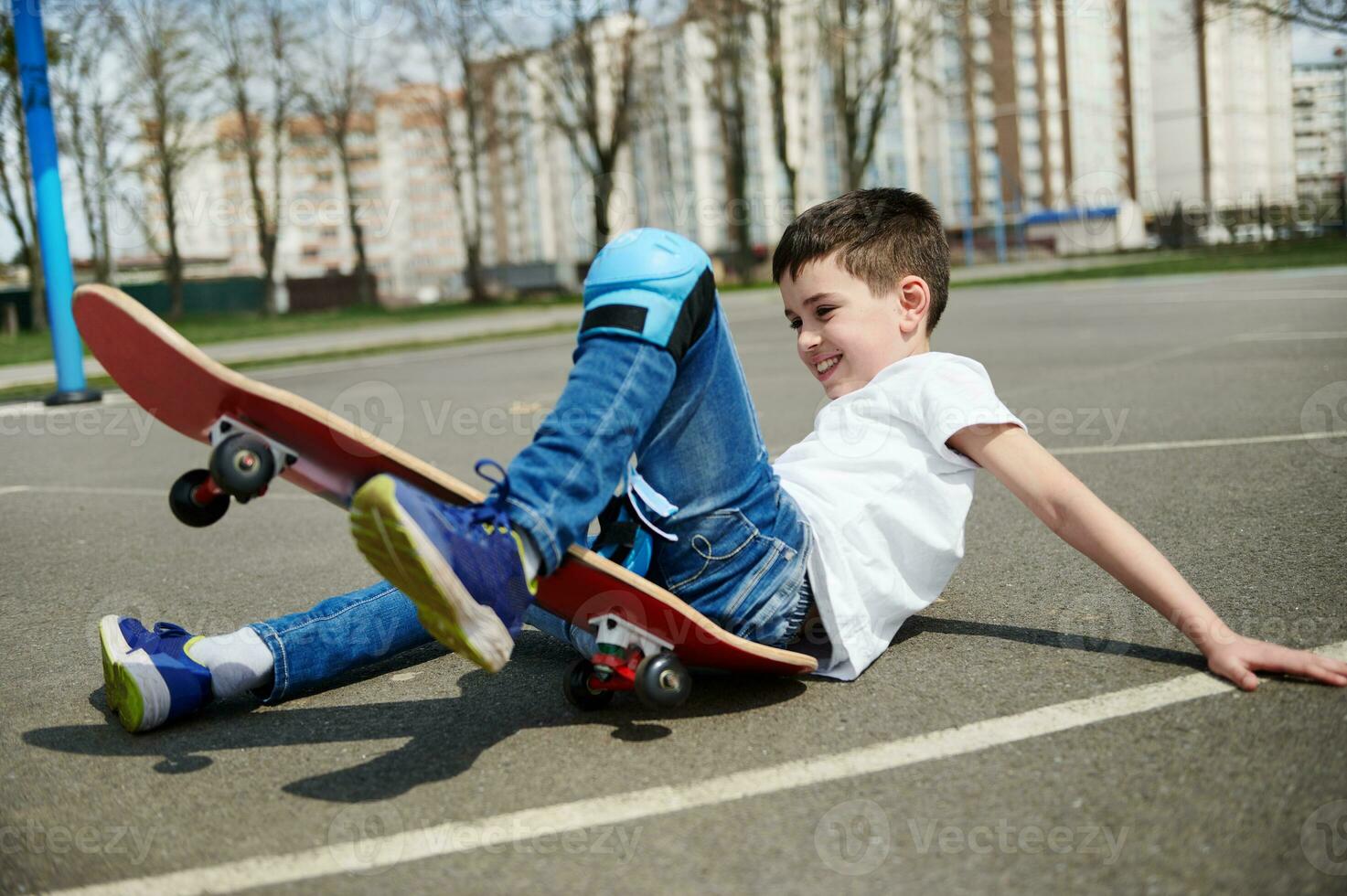 liten pojke gled och föll av de skateboard på de asfalt av de lekplats foto