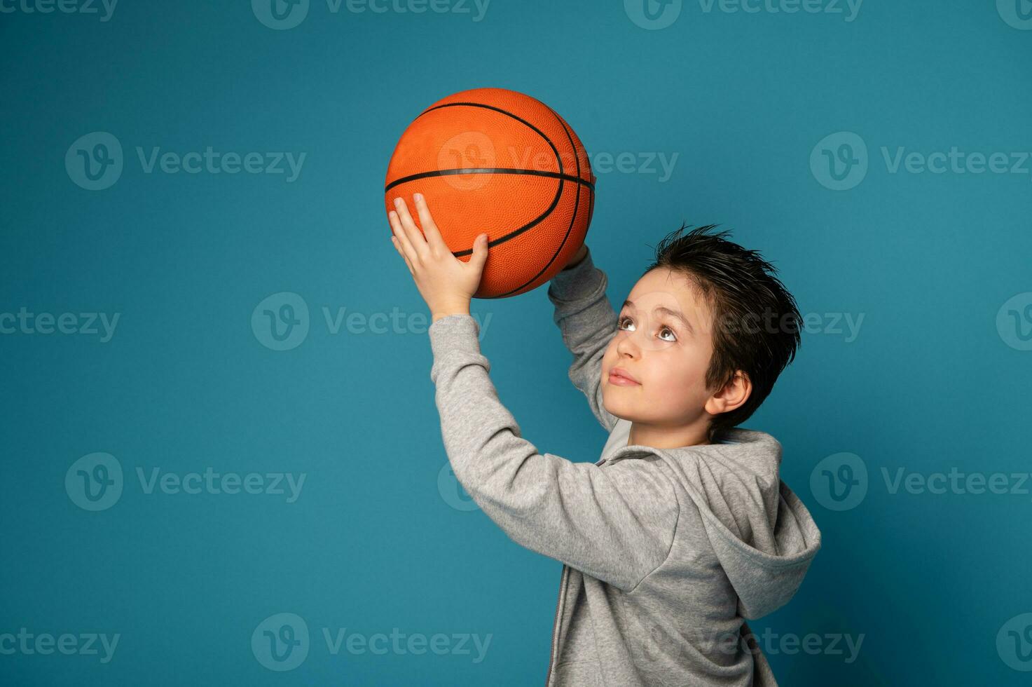 Tonårs pojke, basketboll spelare, Framställ över blå bakgrund med ett orange boll i de händer foto