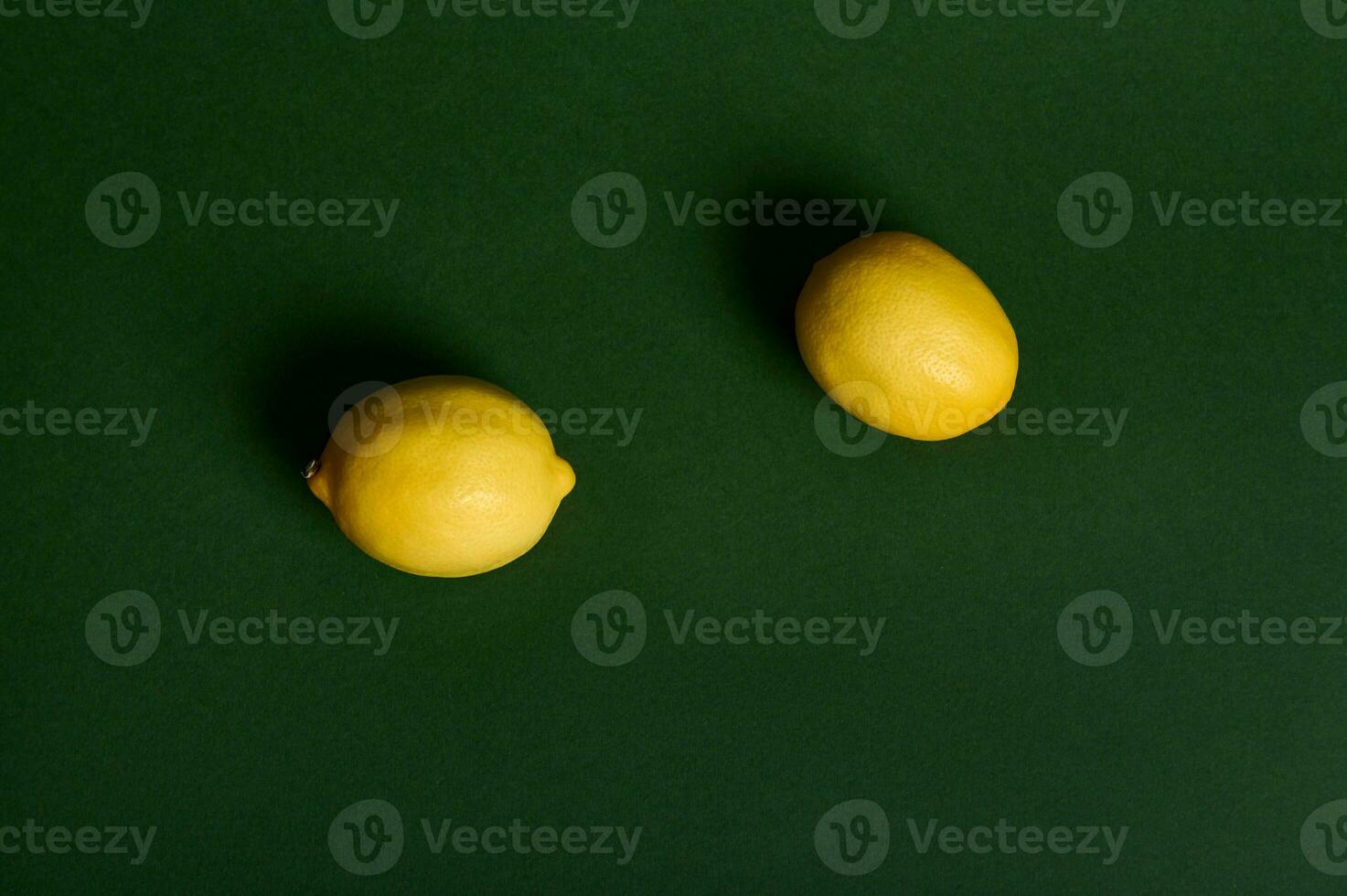 platt lägga sammansättning av två ljus gul citroner på en mörk grön bakgrund , studio skott med mjuk ljus. mat bakgrund. vegan friska äter. kopia Plats för annons foto