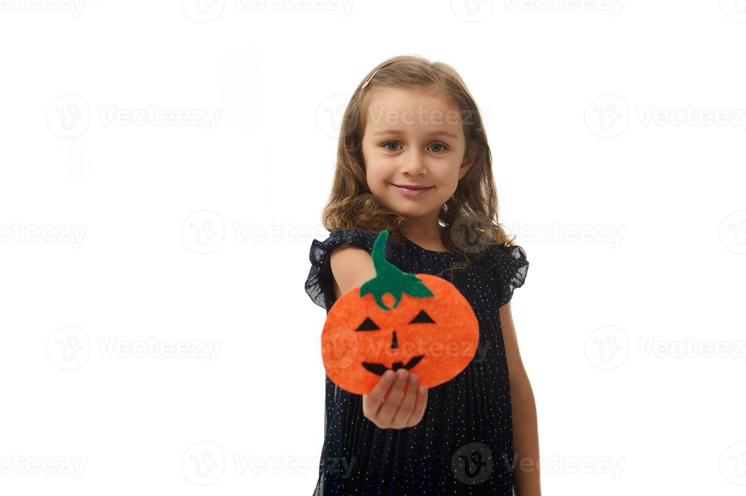 isolerat porträtt på vit bakgrund med kopia Plats av förtjusande liten flicka, 4 år gammal Söt unge, innehav en hemlagad filtskuren pumpa, symbol av de halloween fest, och som visar den till de kamera foto