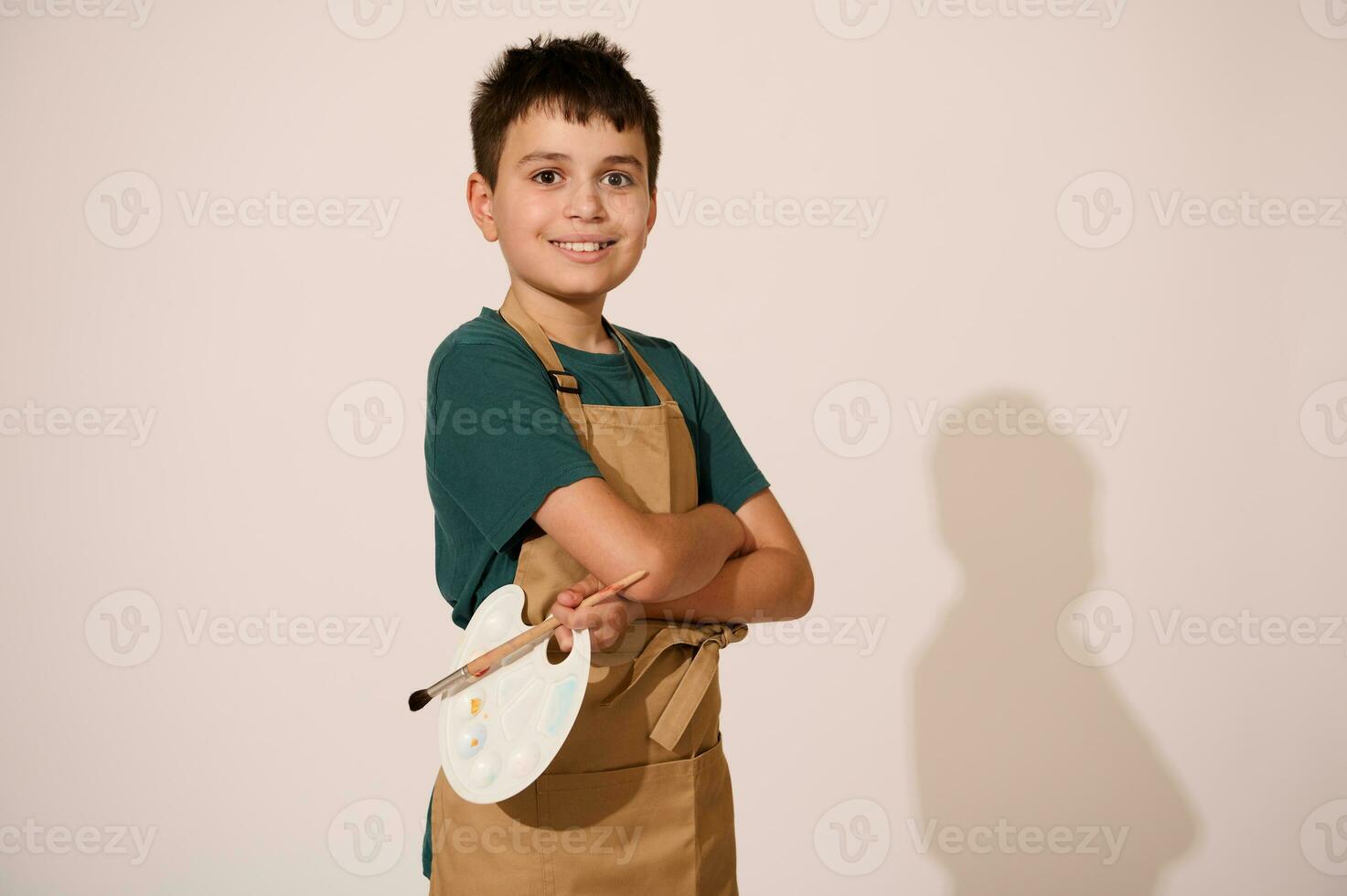 Lycklig skolpojke, målare med vapen vikta, ler på kamera över isolerat studio bakgrund. målning. ungar. hobbies foto