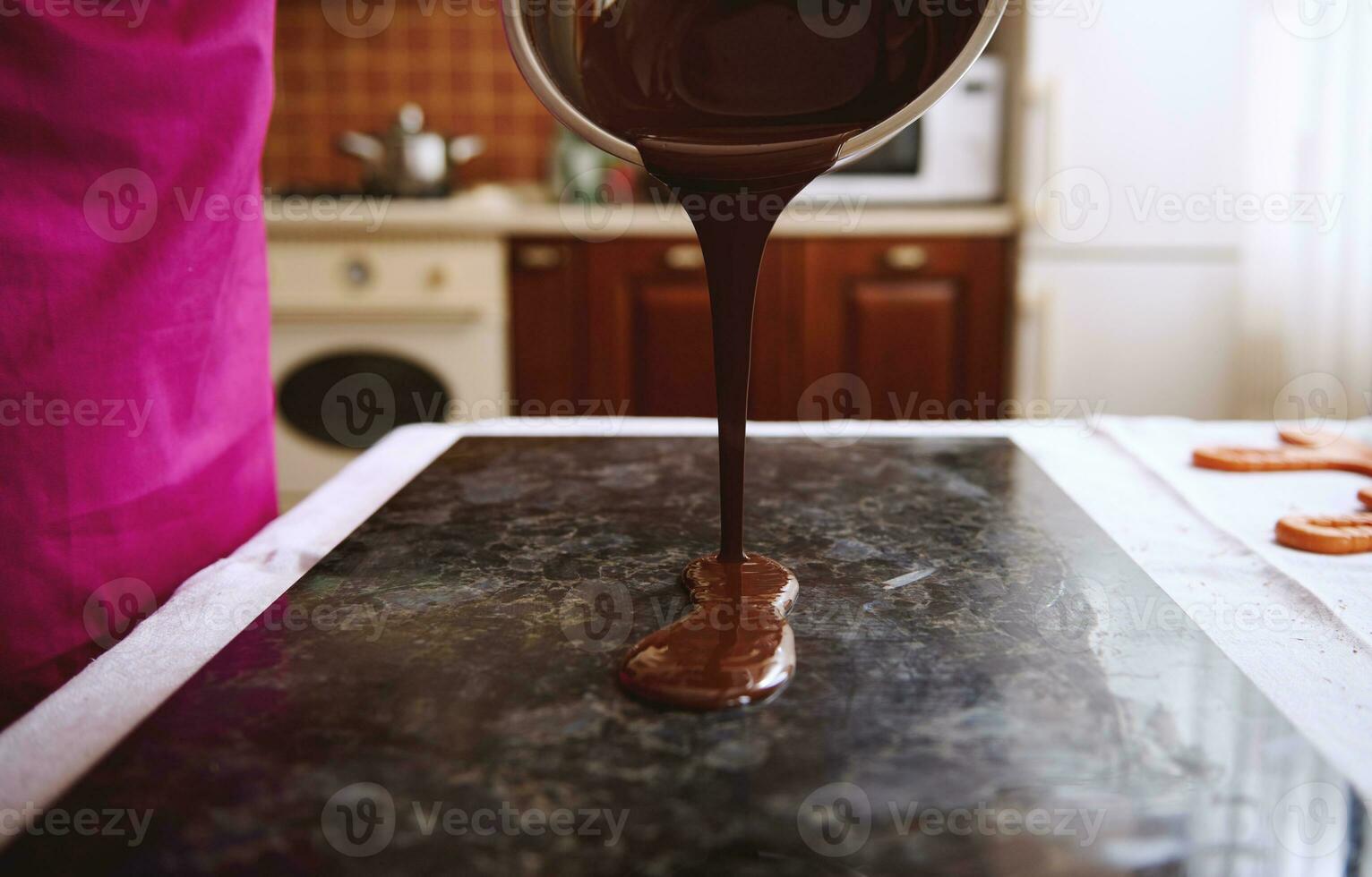 närbild av konditor häller choklad massa in i marmor yta för härdning. foto