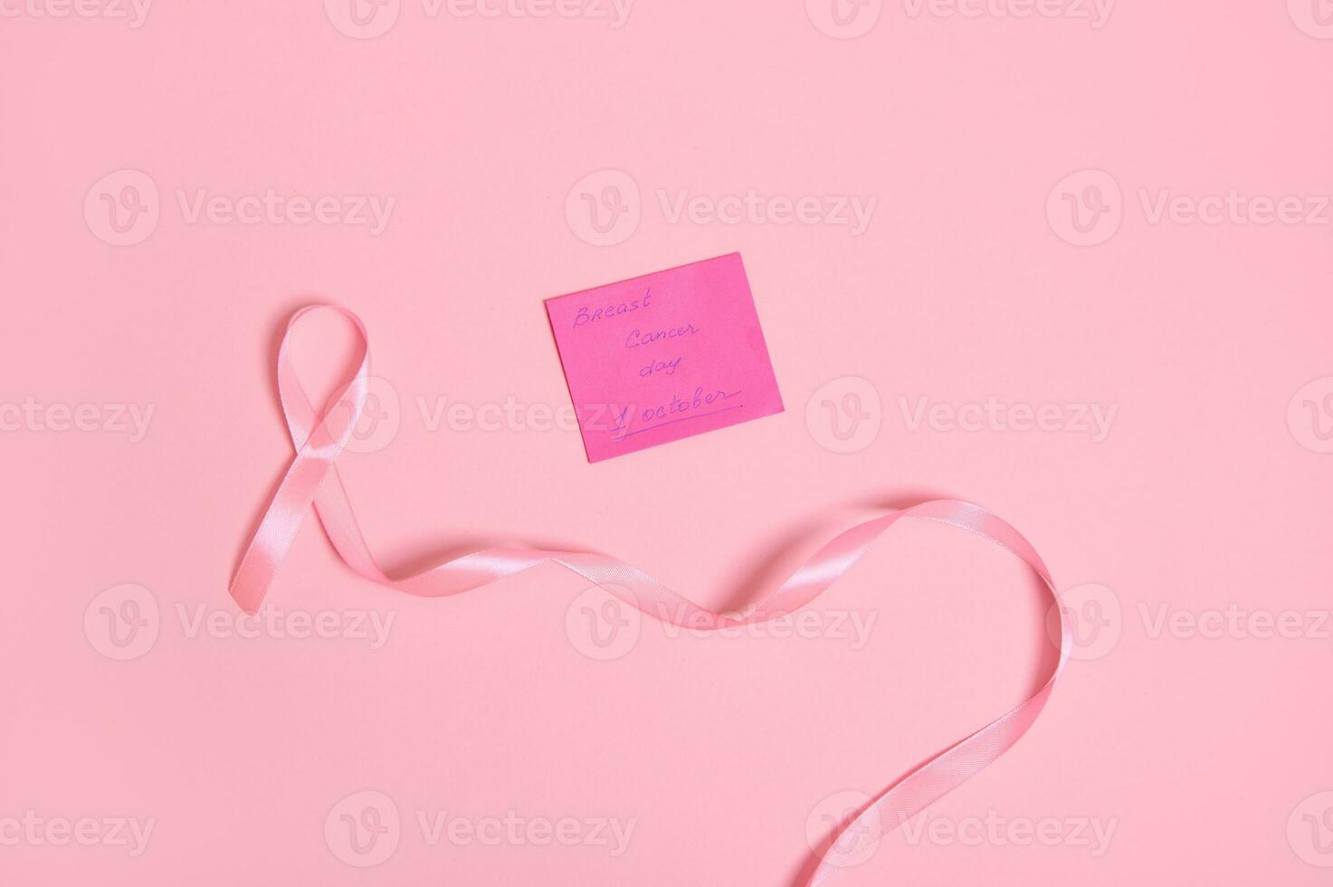 hög vinkel se av en lång rosa band med ändlös ett slutet, och en papper notera med text 1 oktober bröst cancer medvetenhet , isolerat på rosa bakgrund med kopia Plats. platt lägga foto