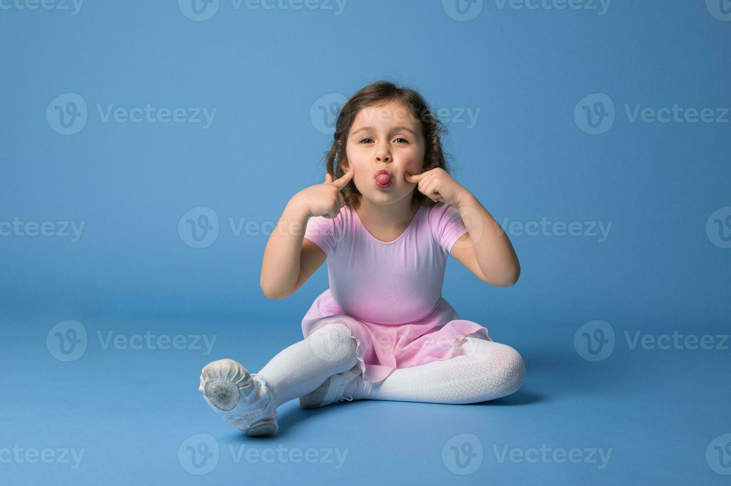 söt ballerina grimaserande och som visar henne tunga ser på kamera, isolerat över blå bakgrund foto