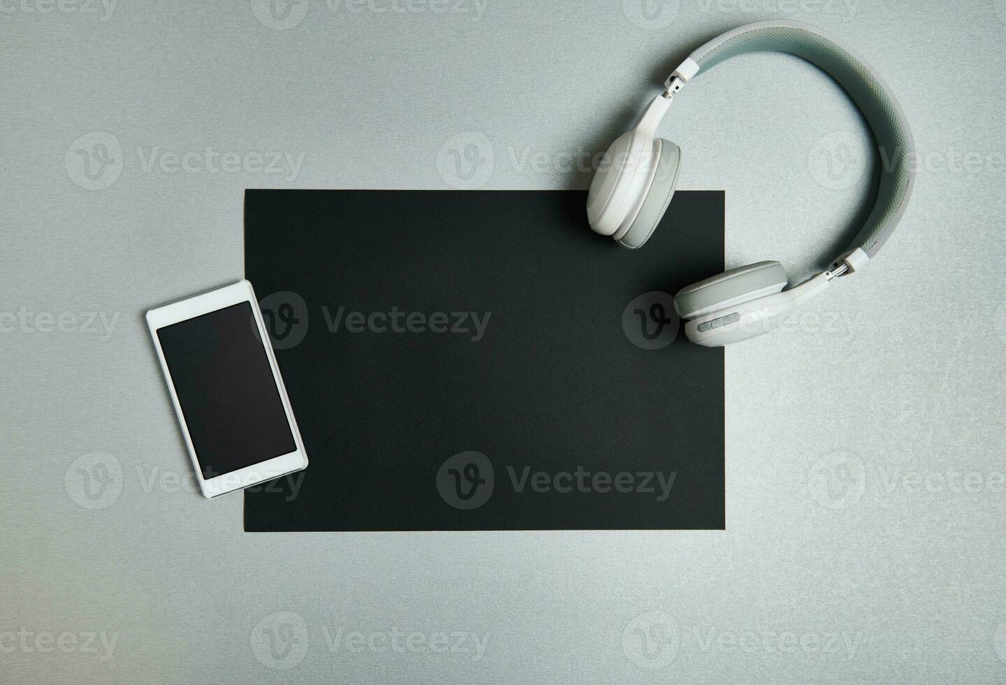 mobil telefon och trådlös hörlurar på en svart ark av papper på en grå bakgrund. svart och vit fortfarande liv. platt lägga . topp se. foto