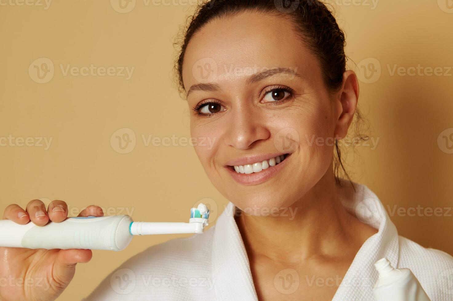isolerat porträtt på beige bakgrund av ett attraktiv kvinna med skön toothy leende innehav en tandborste med tandkräm nära henne ansikte. oral vård begrepp foto