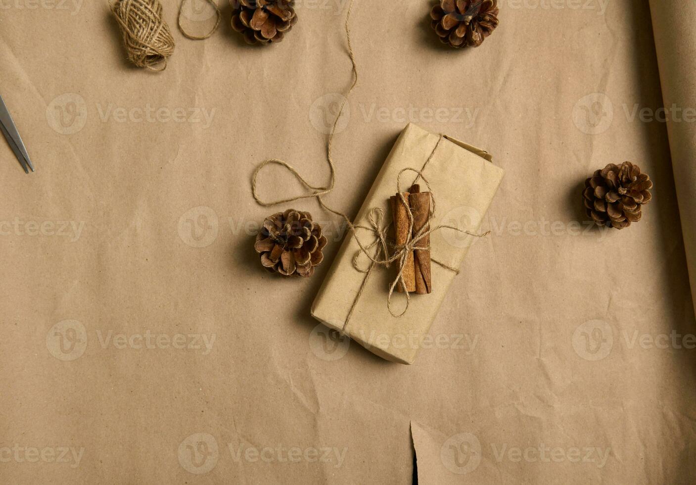 platt lägga minimalistisk sammansättning av en jul närvarande insvept i brun hantverk gåva omslag papper med en rosett tillverkad av rep liggande Nästa till jul träd koner på en kartong bakgrund med kopia Plats foto