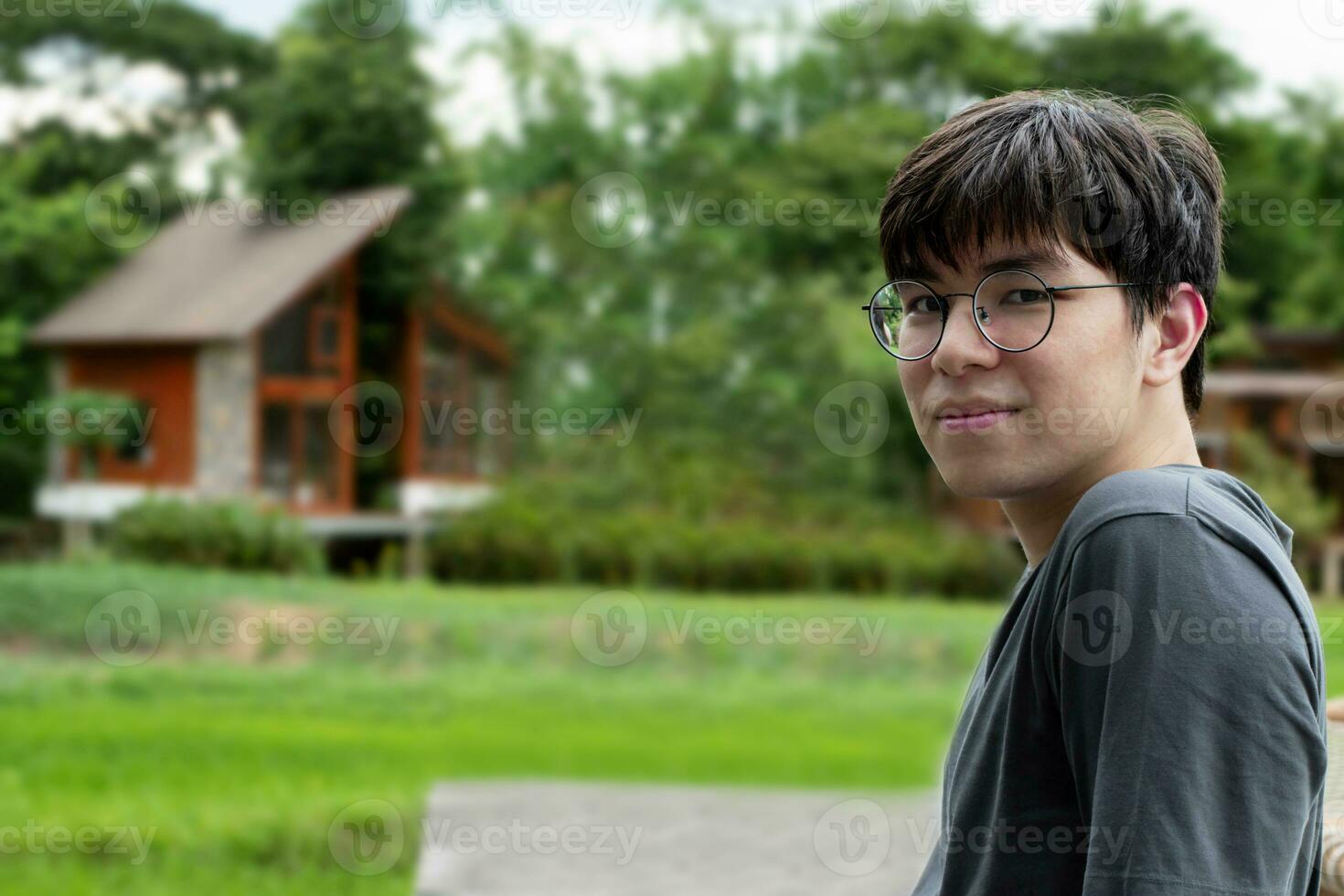 porträtt av ung asiatisk vuxen man bär hörlurar, stående, lyssnande till musik och utgifterna fri tid i främre av hans hus, Bra känsla, ensamhet och Bra tid begrepp. foto