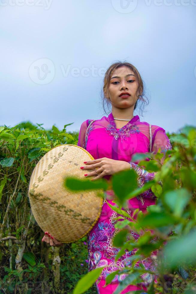 ett indonesiska kvinna i en rosa klänning innehav en bambu hatt i henne händer foto