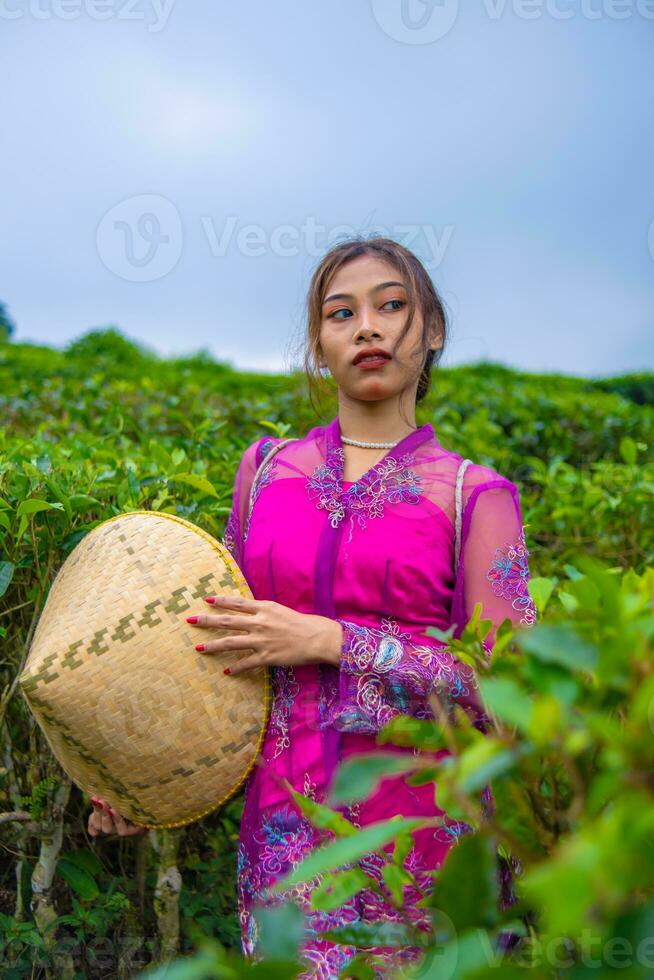 ett indonesiska kvinna i en rosa klänning innehav en bambu hatt i henne händer foto