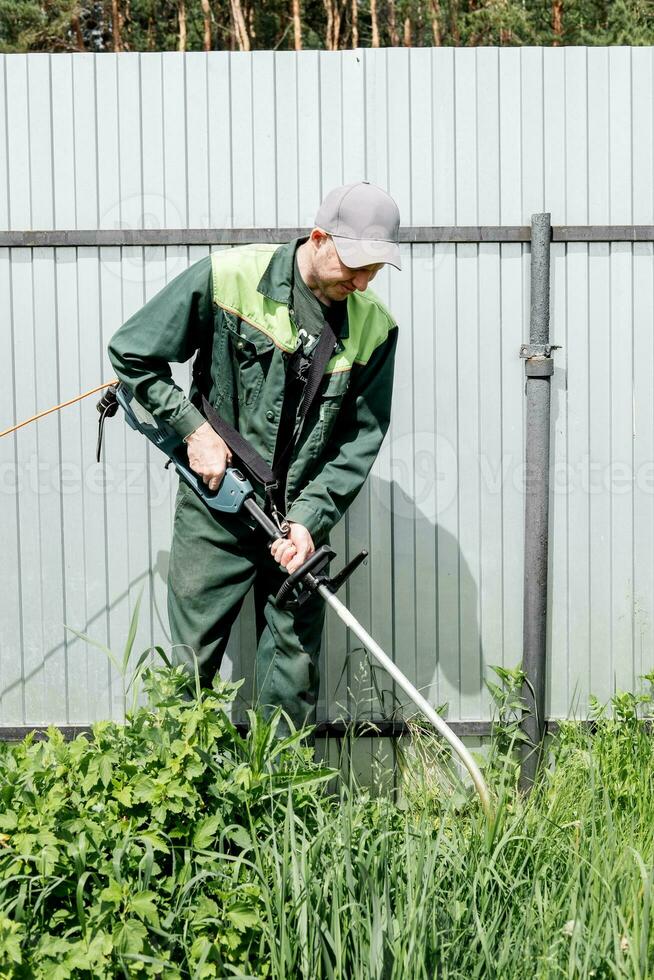 en man klipper gräsmatta gräs med en gräsmatta gräsklippare. bensin gräsmatta gräsklippare, trimmer närbild. man arbetssätt i de trädgård foto