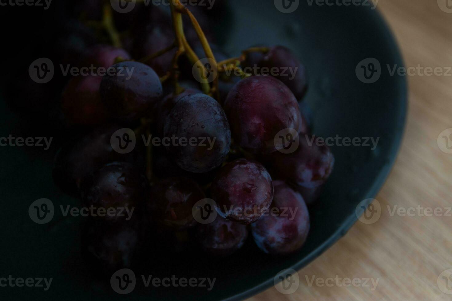 närbild av vindruvor med vatten droppar på en svart keramisk tallrik. foto