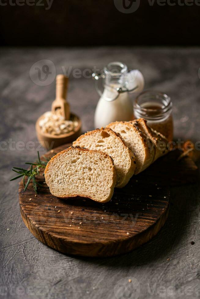 hantverkare bröd hela vete baguette vit mjölk och honung på rustik trä- styrelse och abstrakt tabell. surdeg bröd foto