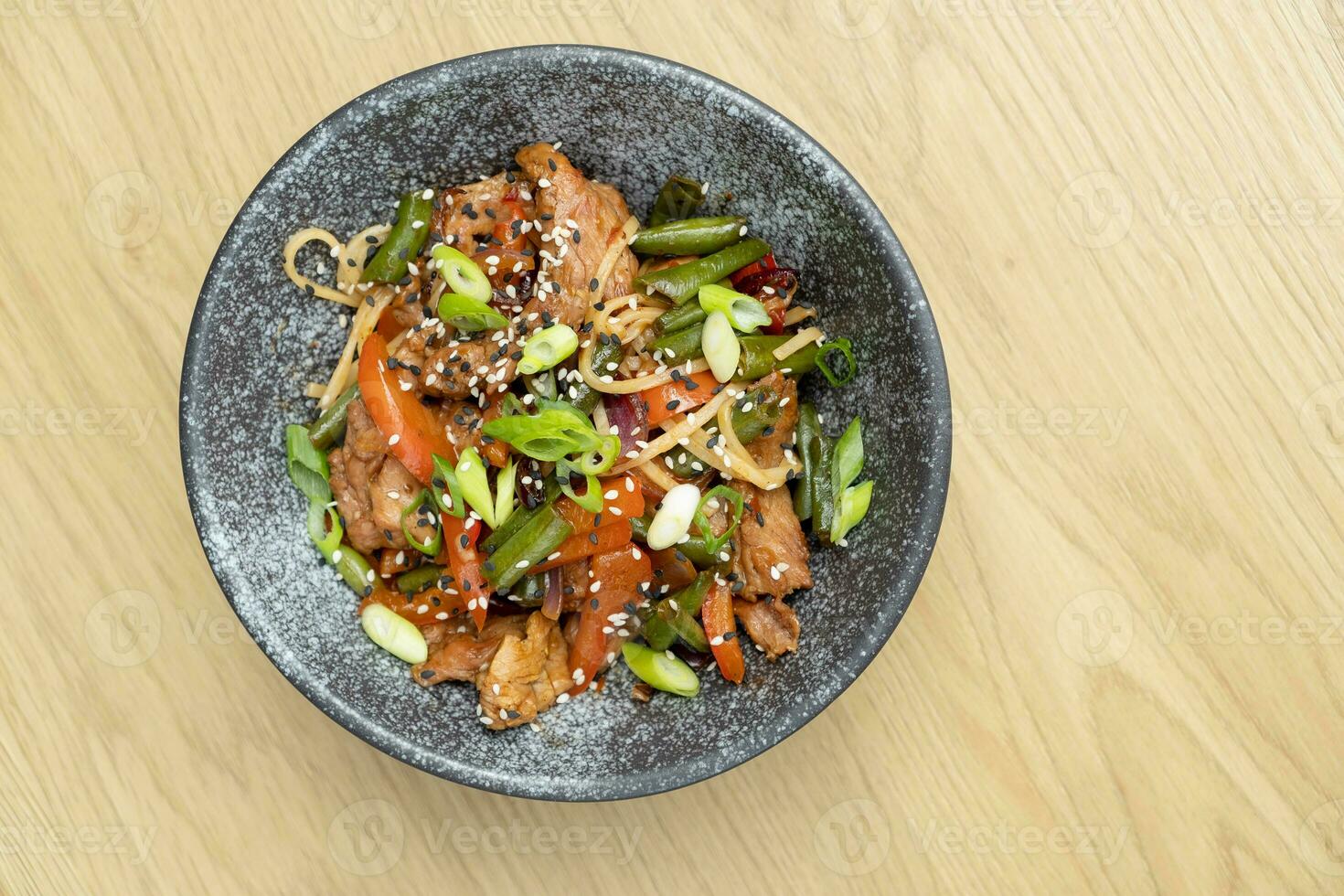 en skål av udon spaghetti, kalvkött och friterad grönsaker topp se på trä- tabell foto