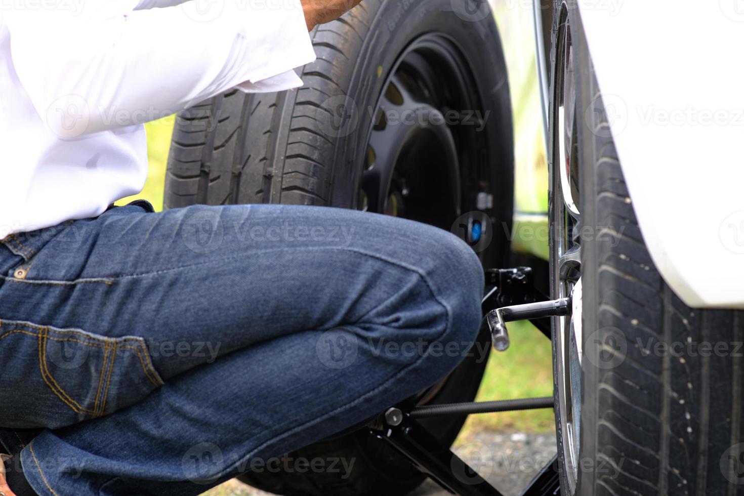 asiatisk ung man som sitter på en trasig bil som ropar på hjälp och reparerade hjulfordon på vägen och ersätter vinter- och sommardäck. säsongsbetonat däckbyte koncept foto