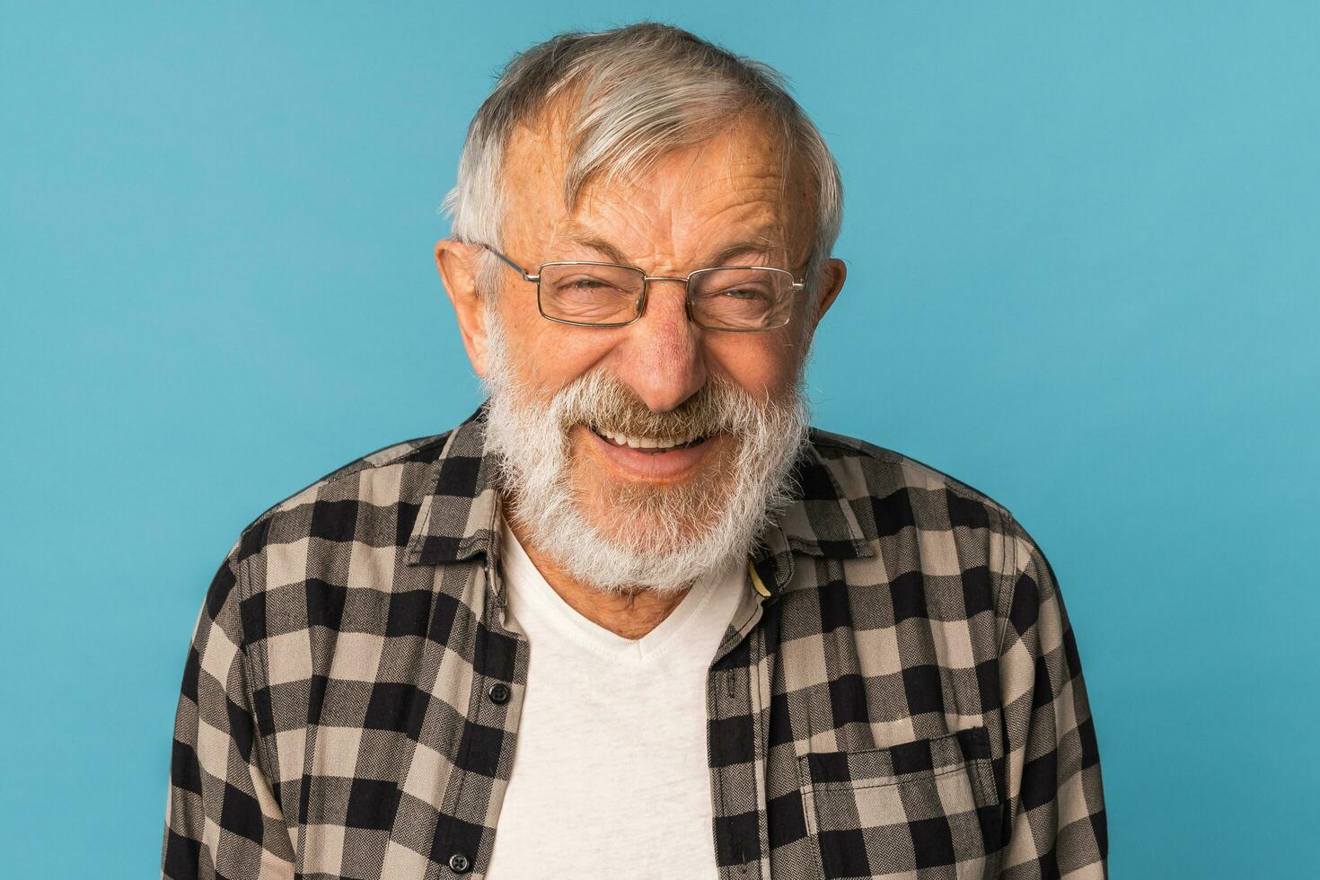 närbild porträtt pensionerad gammal man med vit hår och skägg skratt upphetsad över blå Färg bakgrund foto