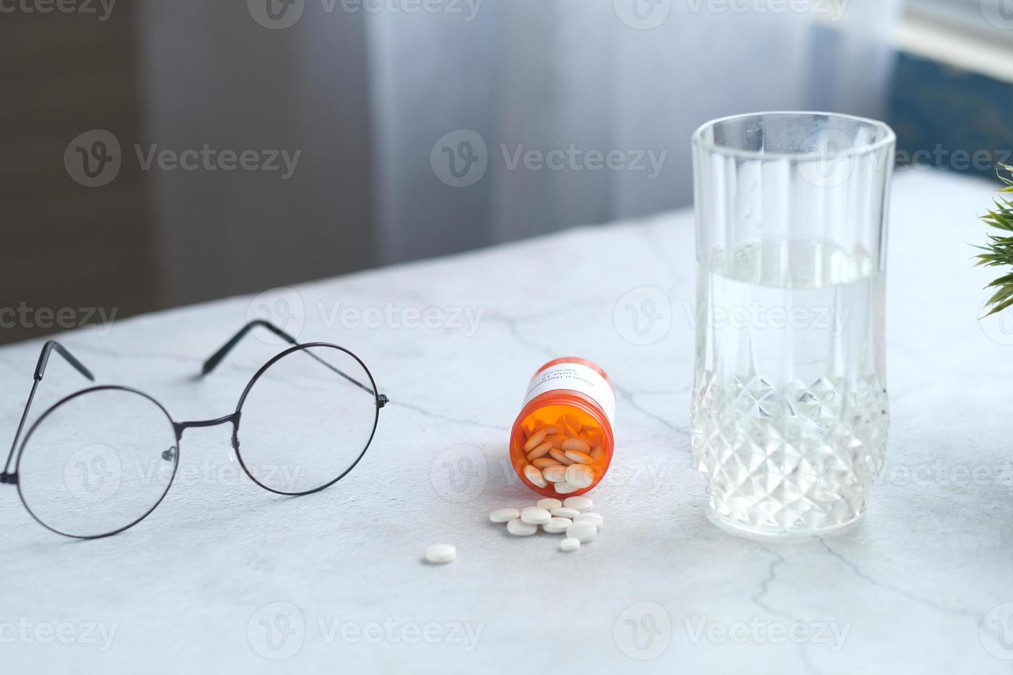 vit färg medicinska piller spilla på bordet med glas vatten och glasögon foto