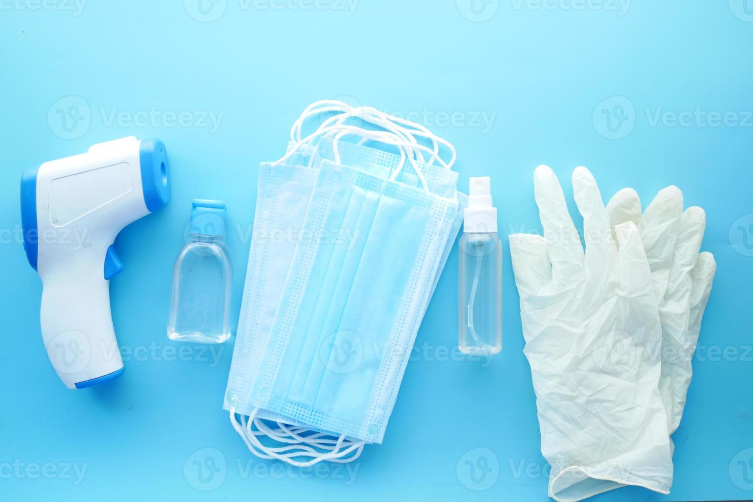 kirurgiska masker, termometer och handdesinfektionsmedel på blå bakgrund. foto