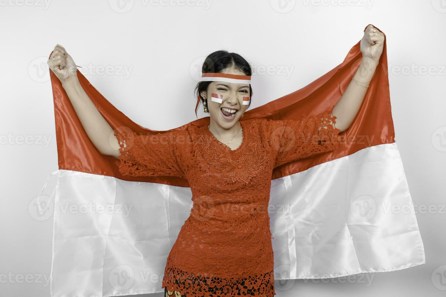 Lycklig leende indonesiska kvinna bär röd kebaya och pannband innehav Indonesiens flagga till fira indonesien oberoende dag isolerat över vit bakgrund. foto