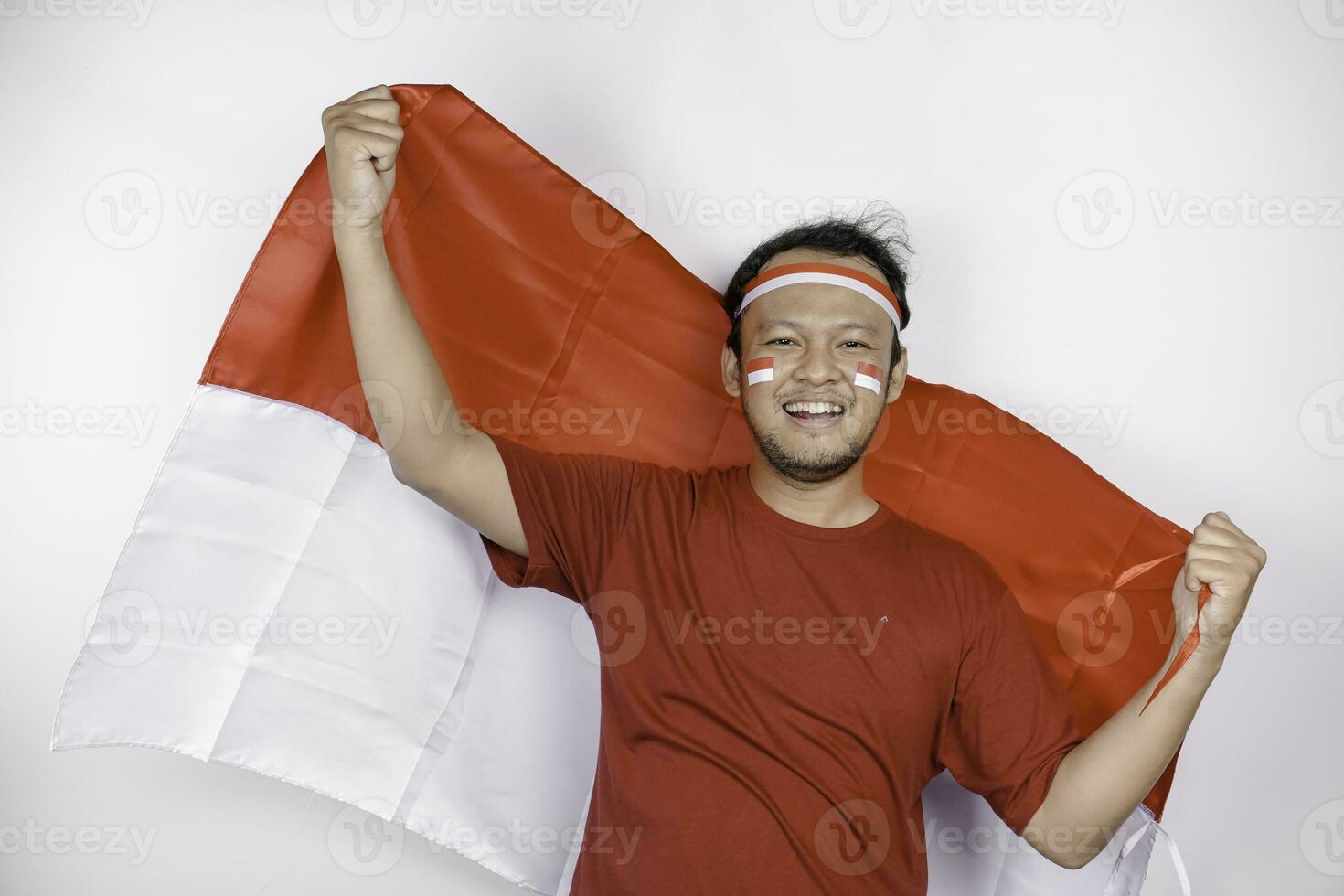 Lycklig leende indonesiska man innehav Indonesiens flagga till fira indonesien oberoende dag isolerat över vit bakgrund. foto