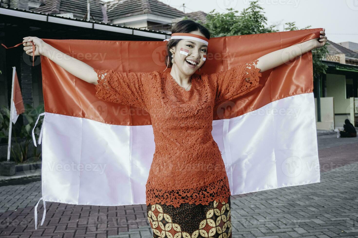 Lycklig leende indonesiska kvinna bär röd kebaya innehav Indonesiens flagga till fira indonesien oberoende dag. utomhus- fotografering begrepp foto