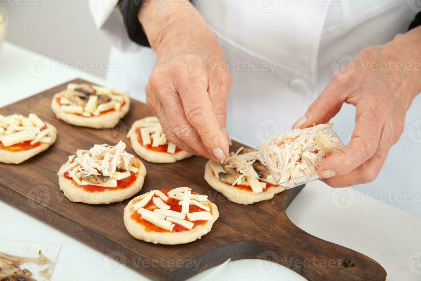 tillsats pålägg till de mini pizzor. tillsats kyckling. utsökt hemlagad mini pizzor förberedelse. foto