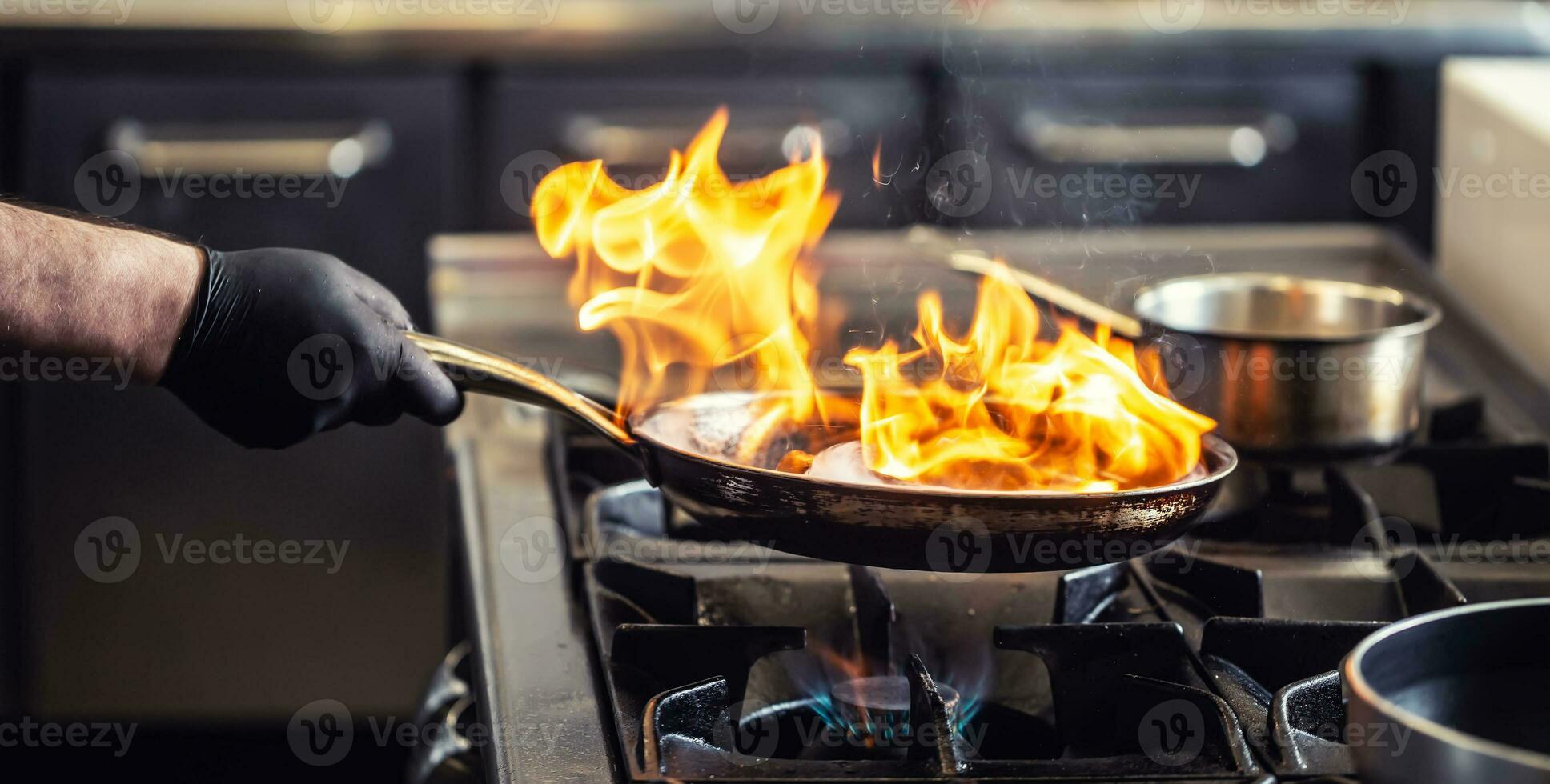 proffs kock flammande i de kök i en panorera på en gaseldad spis foto