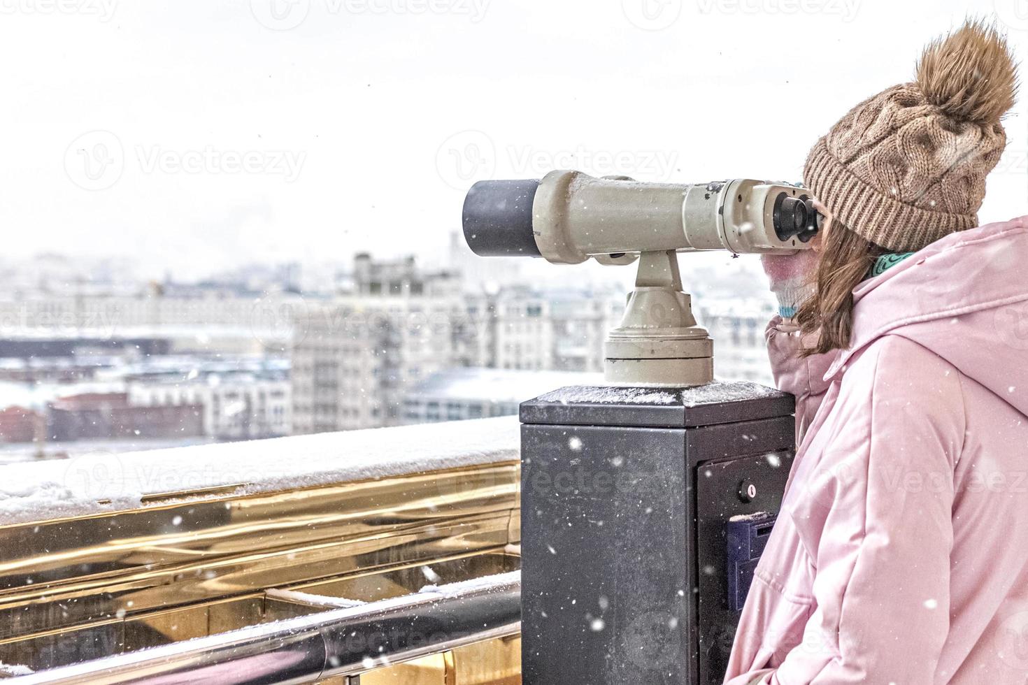 en ung flicka tittar genom myntdrivna kikare på observationsdäcket med utsikt över staden foto