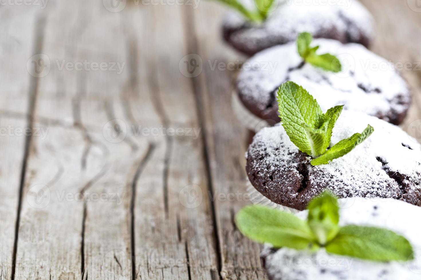 färska choklad mörka muffins med sockerpulver och mynta blad på rustika träbord bakgrund. foto