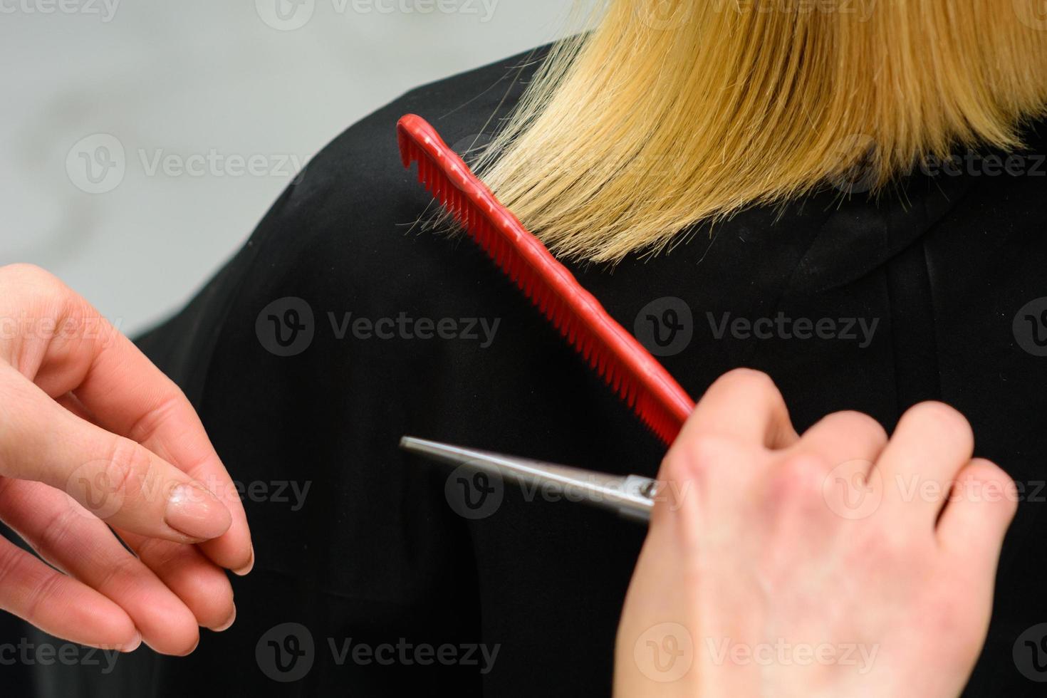 kvinnlig frisör håller i handen mellan fingrar blont hår, kam och sax på nära håll, räta ut hårspetsar. foto