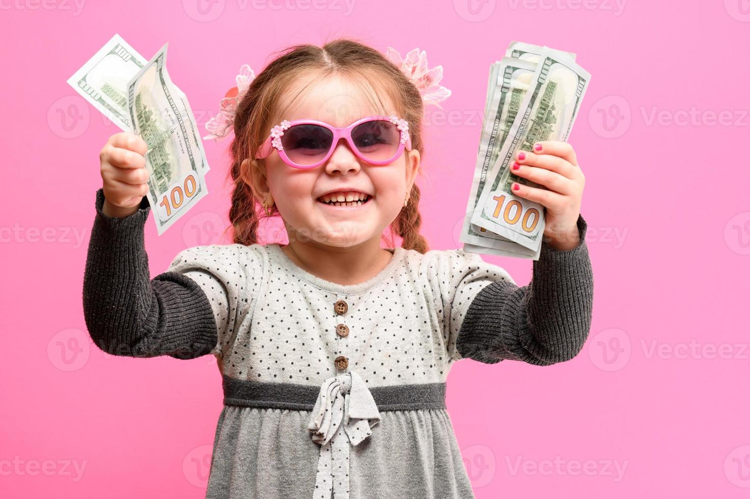 liten flicka i glas med ett paket och pengar på en rosa bakgrund, barn och shopping. foto