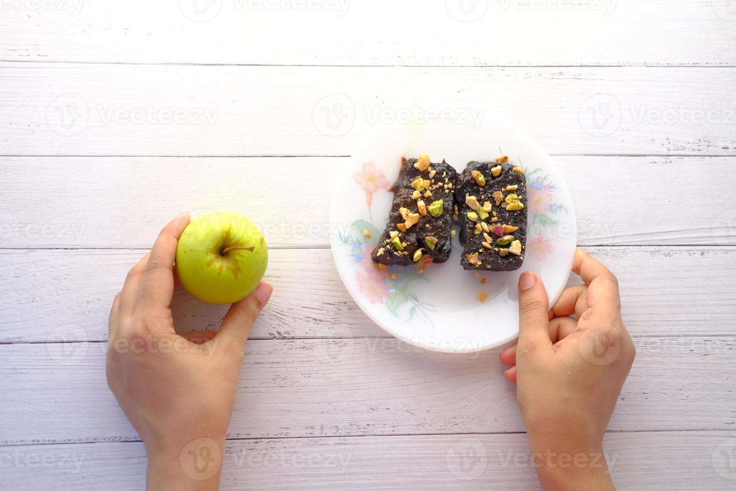 handhåll äpple och brownie på tallriken på bordet foto