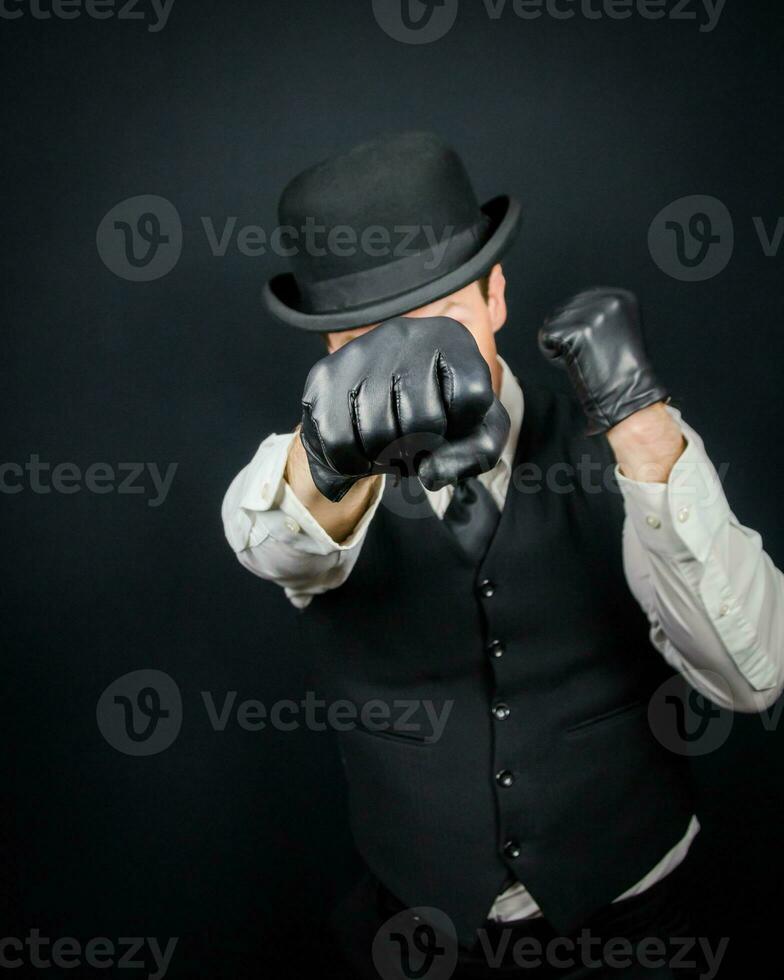 porträtt av farlig årgång kämpe i väst och kastare hatt stående i karate hållning. gangster i svart läder handskar. foto