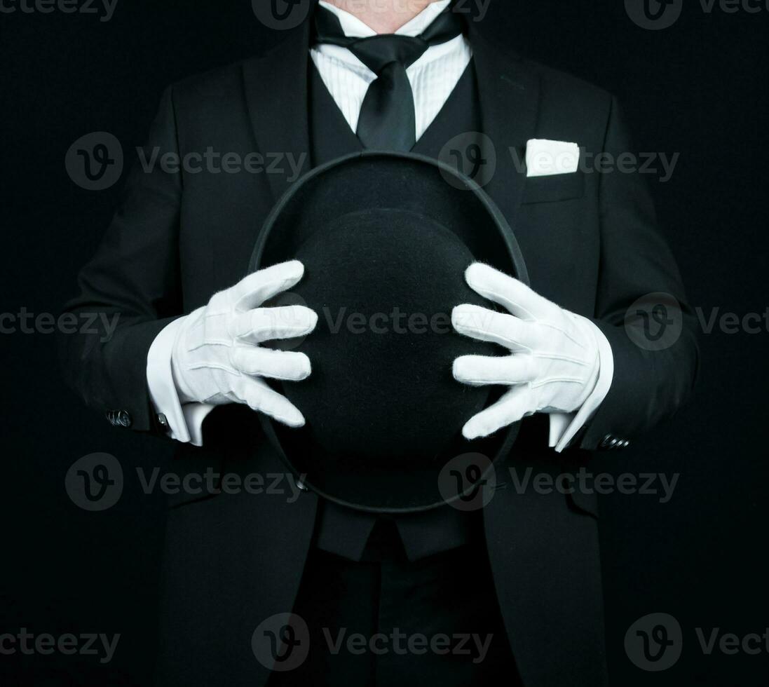 porträtt av butler i mörk formell kostym och vit handskar innehav en kastare hatt. begrepp av service industri och professionell artighet. foto