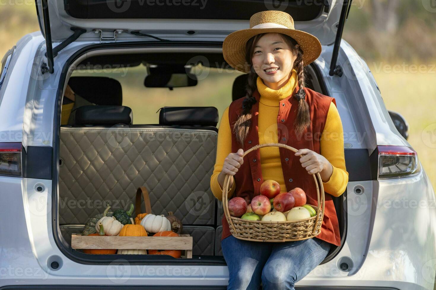 Lycklig asiatisk jordbrukare flicka bärande producera skörda med hemodlade organiska ämnen äpple, squash och pumpa Sammanträde på de bil trunk på lokal- bruka marknadsföra under höst säsong för lantbruk produkt begrepp foto