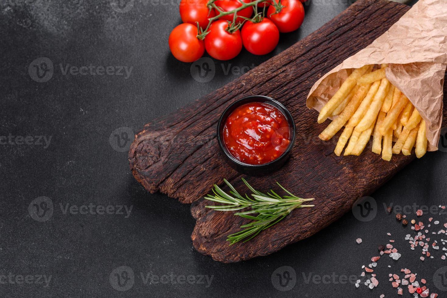 färska välsmakande pommes frites och röd sås på en träskärbräda foto