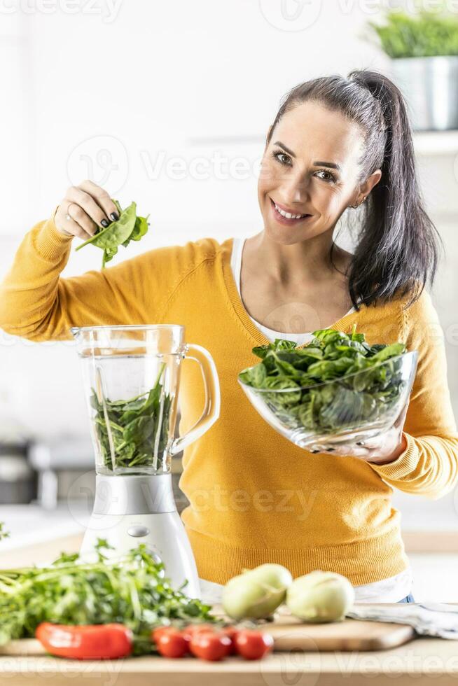 leende kvinna framställning spenat smoothie, sätta löv i blandare. foto