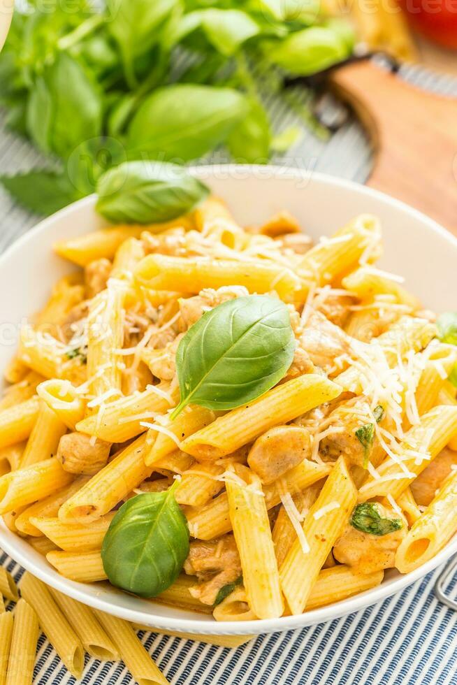 pasta penne med kyckling bitar svamp basilika parmesan ost och vit vin. italiensk mat i vit tallrik på kök tabell foto