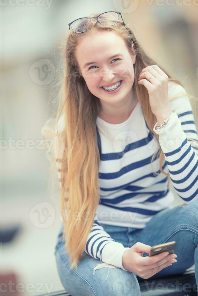 porträtt av en leende skön Tonårs flicka med dental tandställning. ung skol med skola väska och mobil telefon foto