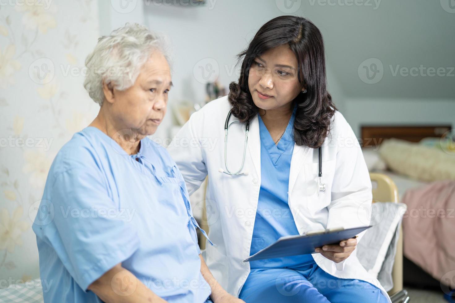 läkare som talar om diagnos och anmärkning på Urklipp med asiatisk senior eller äldre gammal damkvinna medan du ligger på sängen på vårdavdelningen, hälsosamt starkt medicinskt koncept. foto