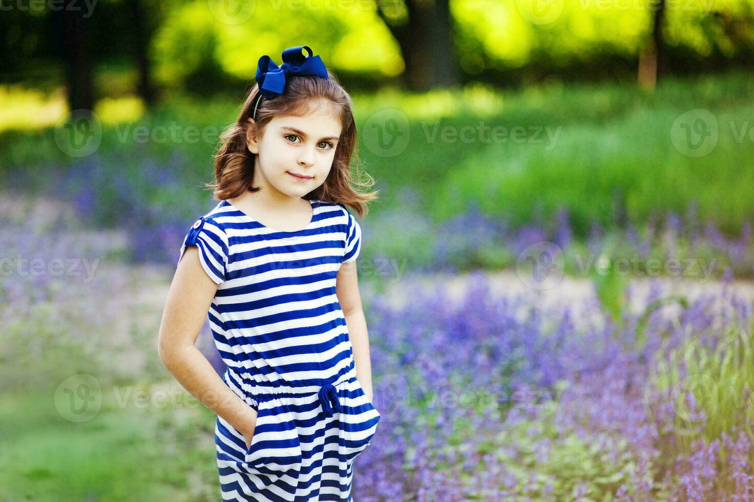 en liten flicka i en randig klänning stående i en fält av lavendel- foto